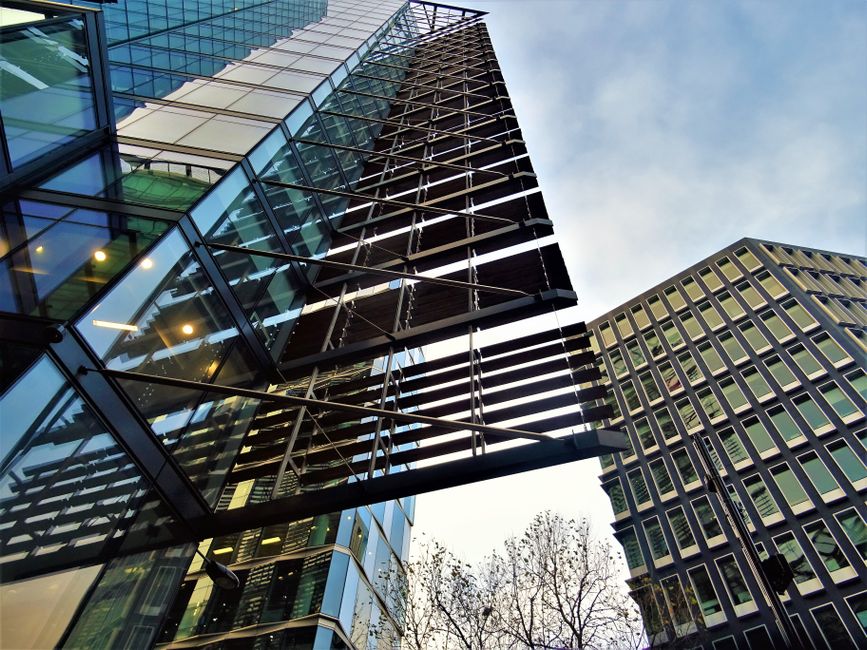 A modern commercial office building with a curved glass facade, consisting of large, reflective blue-tinted glass panels and metal framing. The building's exterior appears clean and well-maintained, w